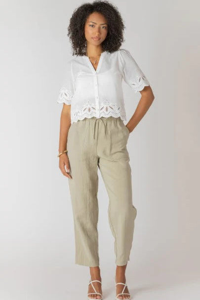 Woman wearing a white blouse with lace details and beige pants on a plain background