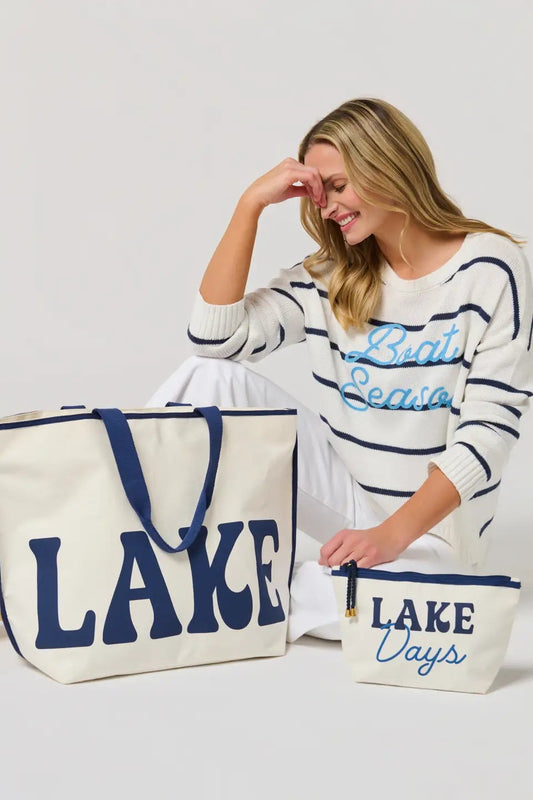 Woman holding two tote bags with 'LAKE DAYS' text, wearing a striped sweater.