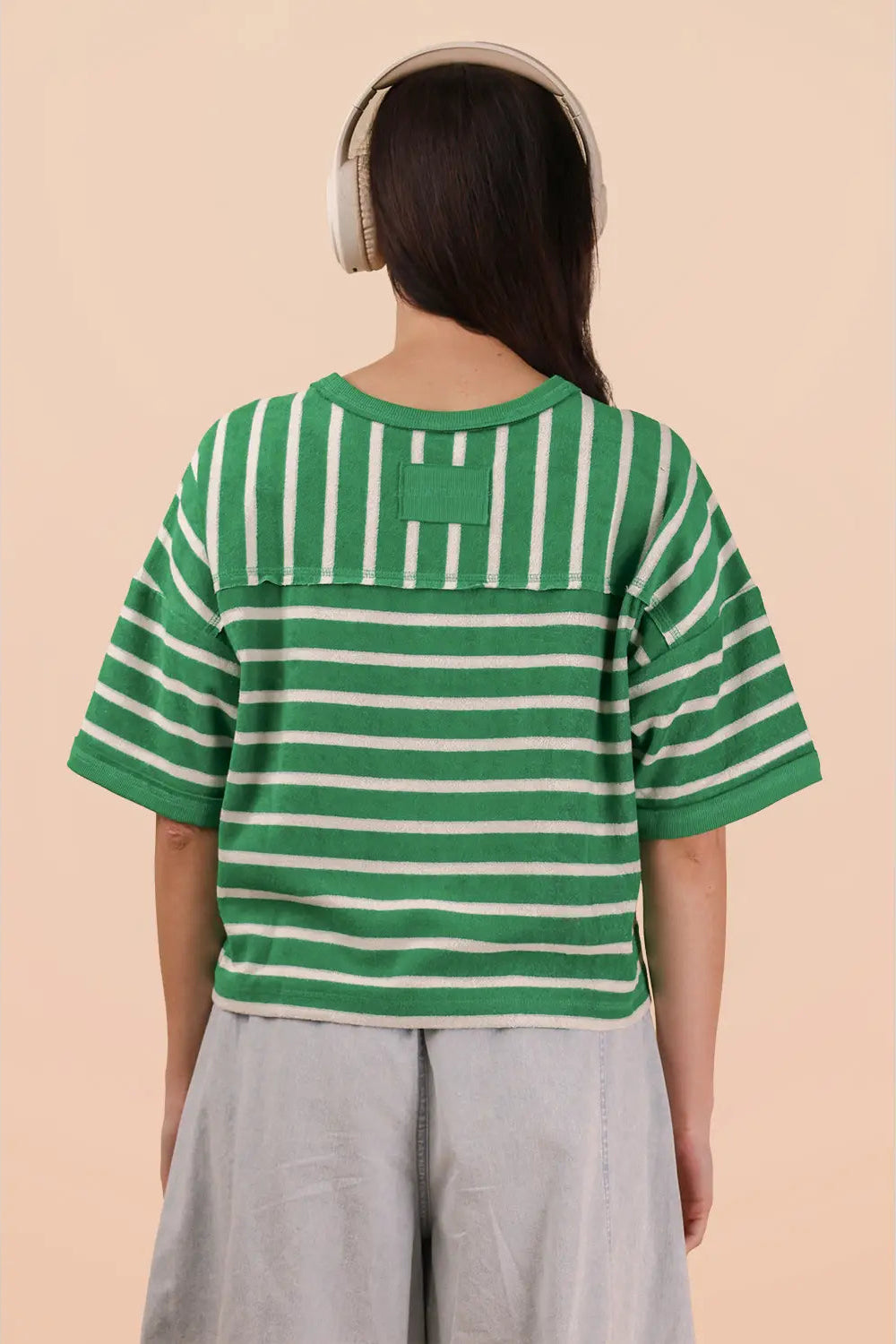 Person wearing a green and white striped shirt with a logo on a beige background