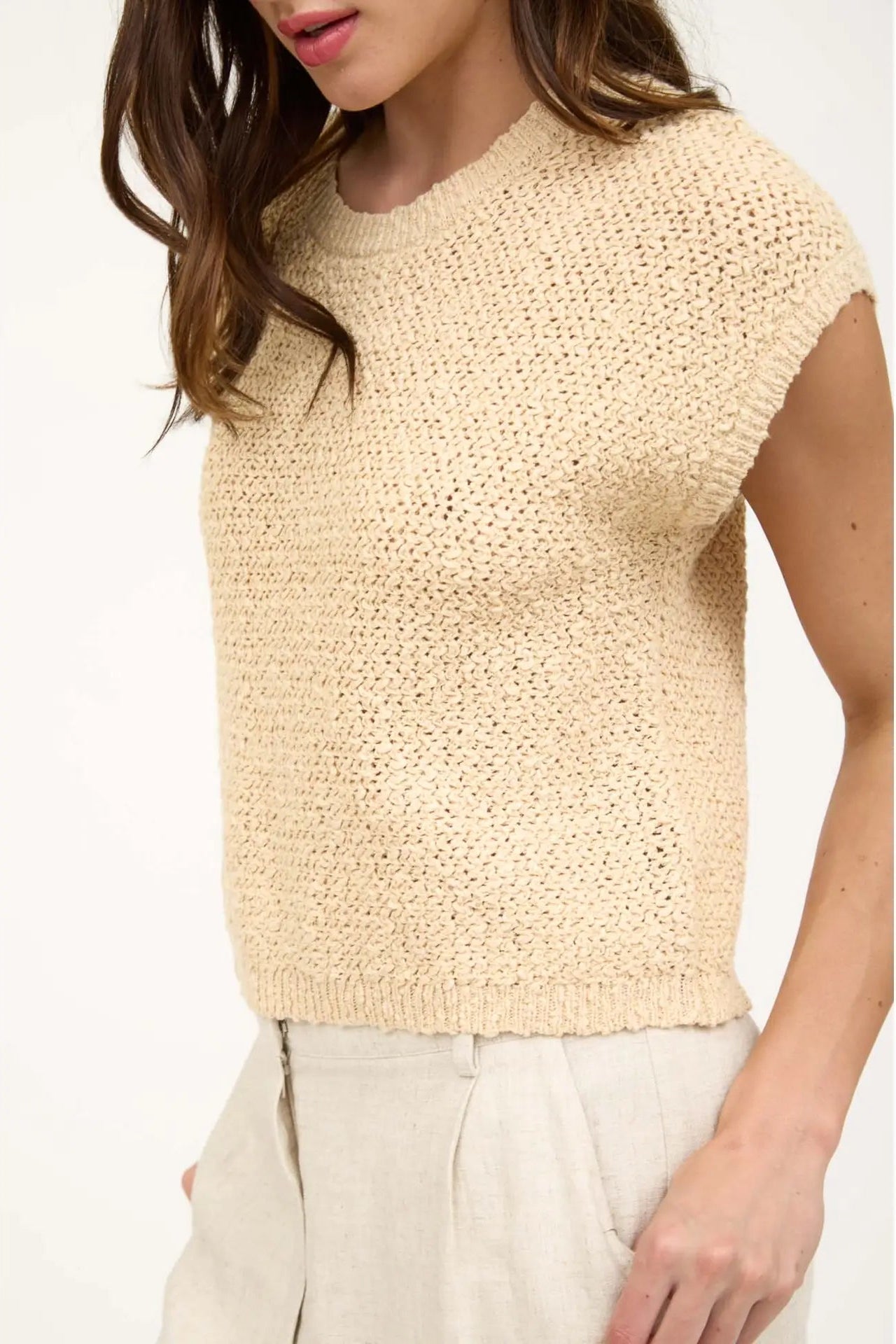 Beige knitted sleeveless top worn by a person on a white background