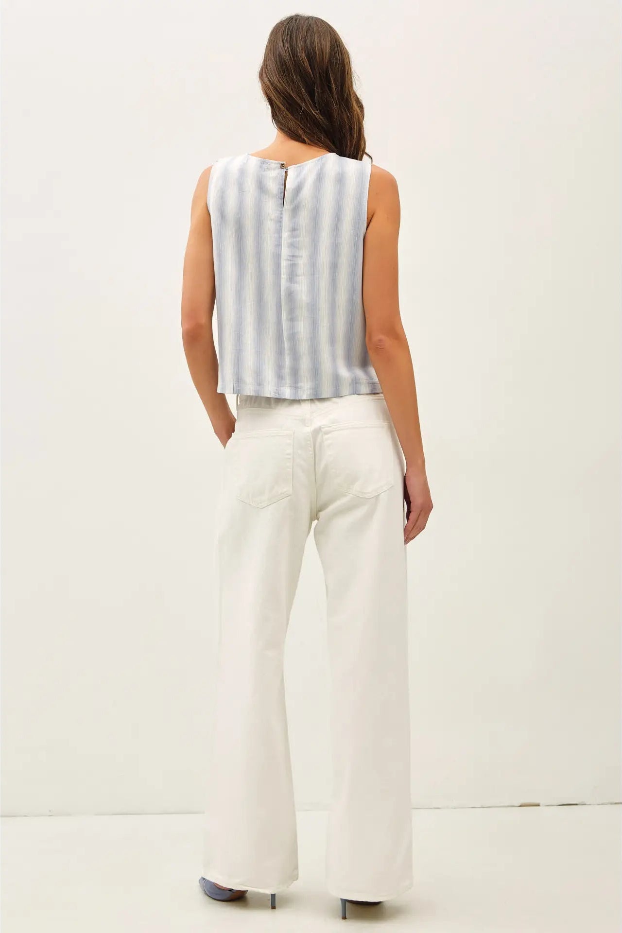 Woman wearing a sleeveless striped top and white pants on a plain background