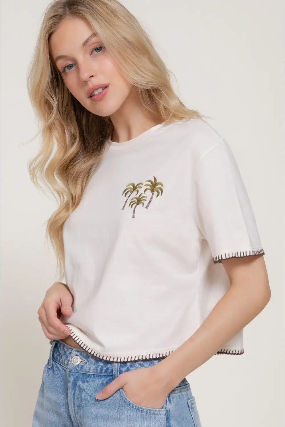 Woman wearing a white t-shirt with palm tree design and blue jeans on a plain background