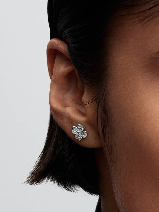 Close-up of an ear wearing a silver floral earring against a neutral background