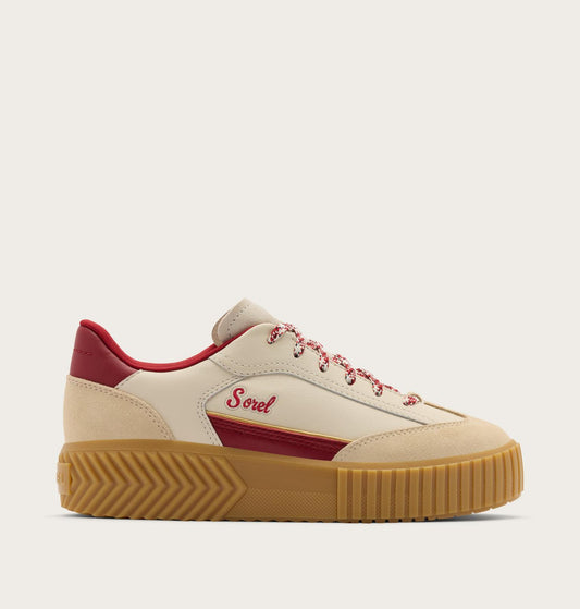 A low-top platform sneaker by Sorel in beige suede and leather, featuring a chunky tan gum sole, red heel and side accents, and red laces, shown against a light beige background.