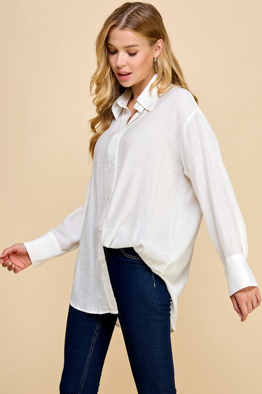 Woman wearing a white blouse and dark jeans against a beige background