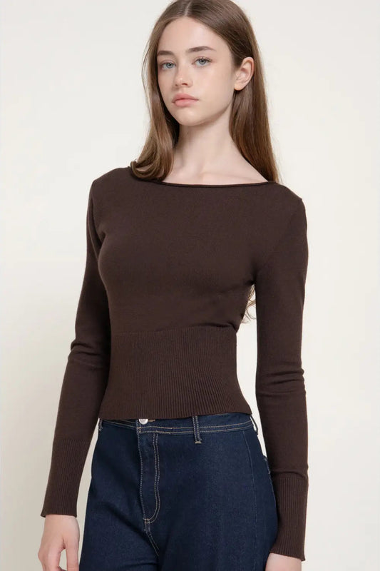 A woman modeling a dark brown long-sleeve knit top with a wide boat neckline, paired with dark blue jeans, against a plain off-white background.