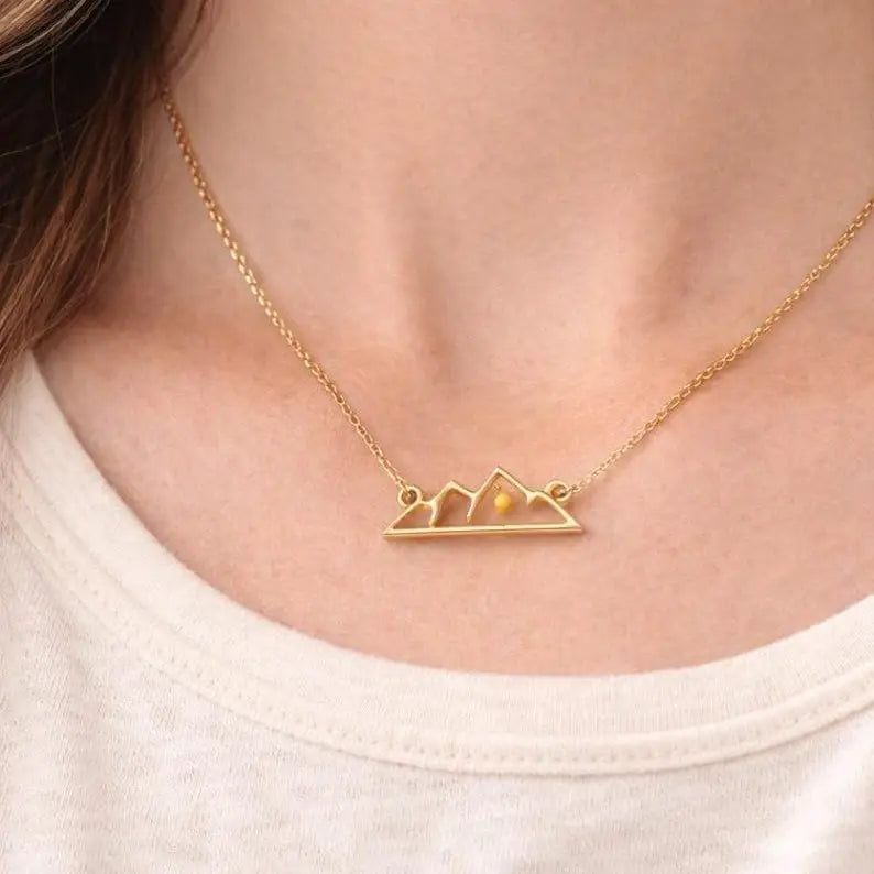 Gold necklace with mountain design on a person wearing a white shirt