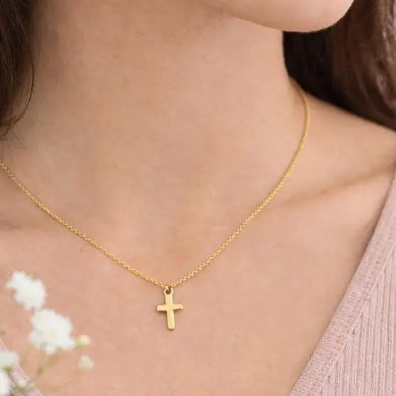 Gold necklace with a cross pendant worn by a person, with a blurred background.