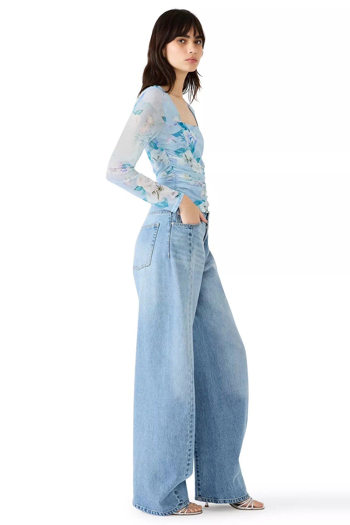 Woman wearing a light blue floral top and wide-leg jeans on a white background