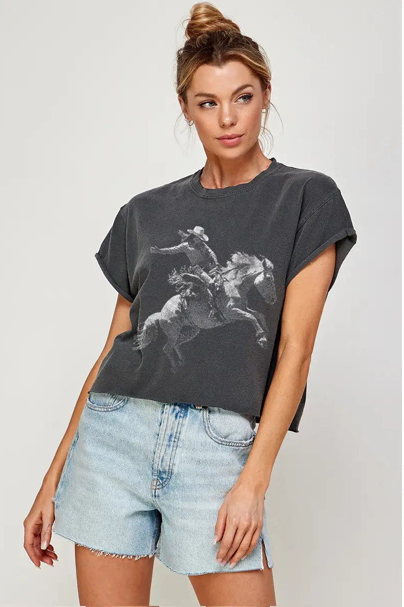 Woman wearing a dark gray t-shirt with a graphic design and light blue denim shorts on a plain background