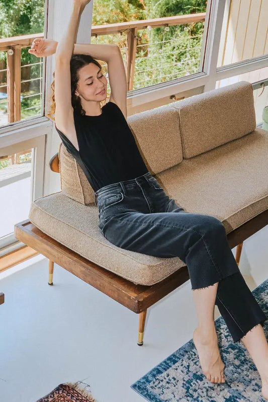 Woman stretching on a modern sofa in a bright living room with large windows.