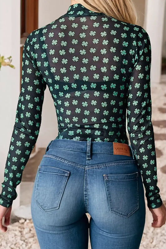 Person wearing a black long-sleeve shirt with green shamrock pattern and blue jeans.