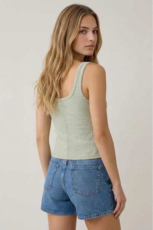 Woman wearing a light green ribbed tank top and blue denim shorts on a plain background