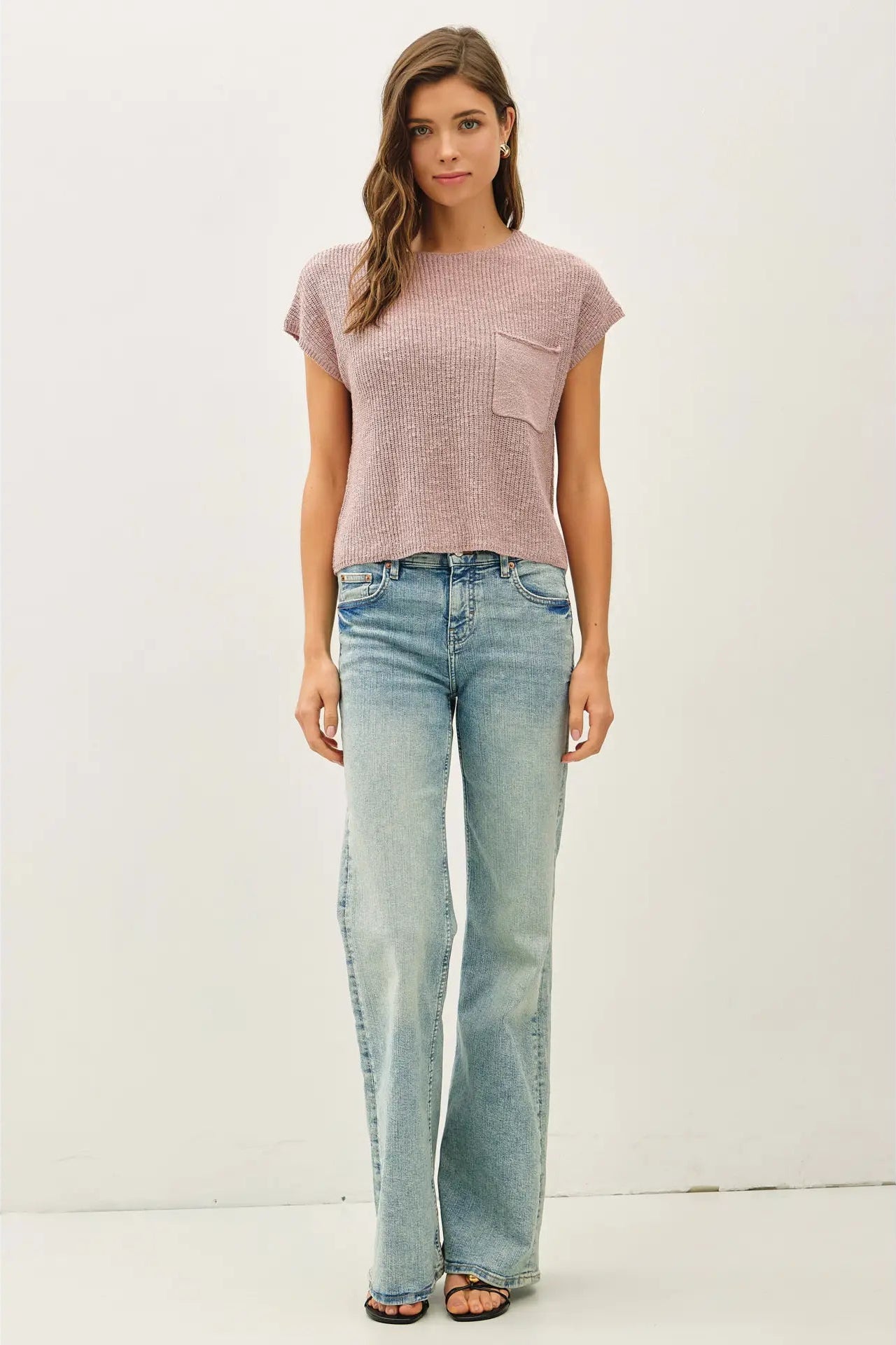 Woman wearing a pink textured top and light blue jeans on a white background
