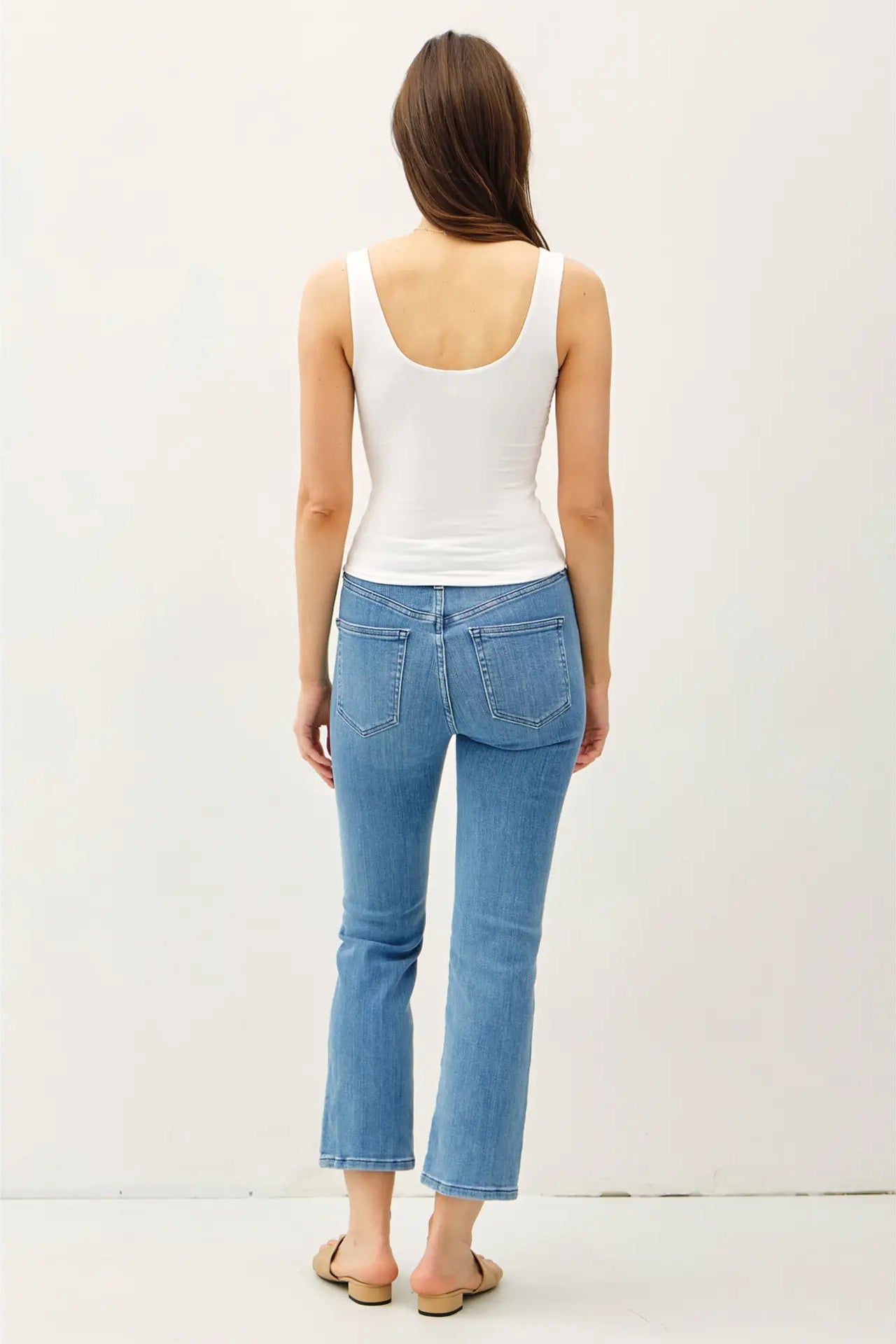 Woman wearing a white tank top and blue jeans on a plain background