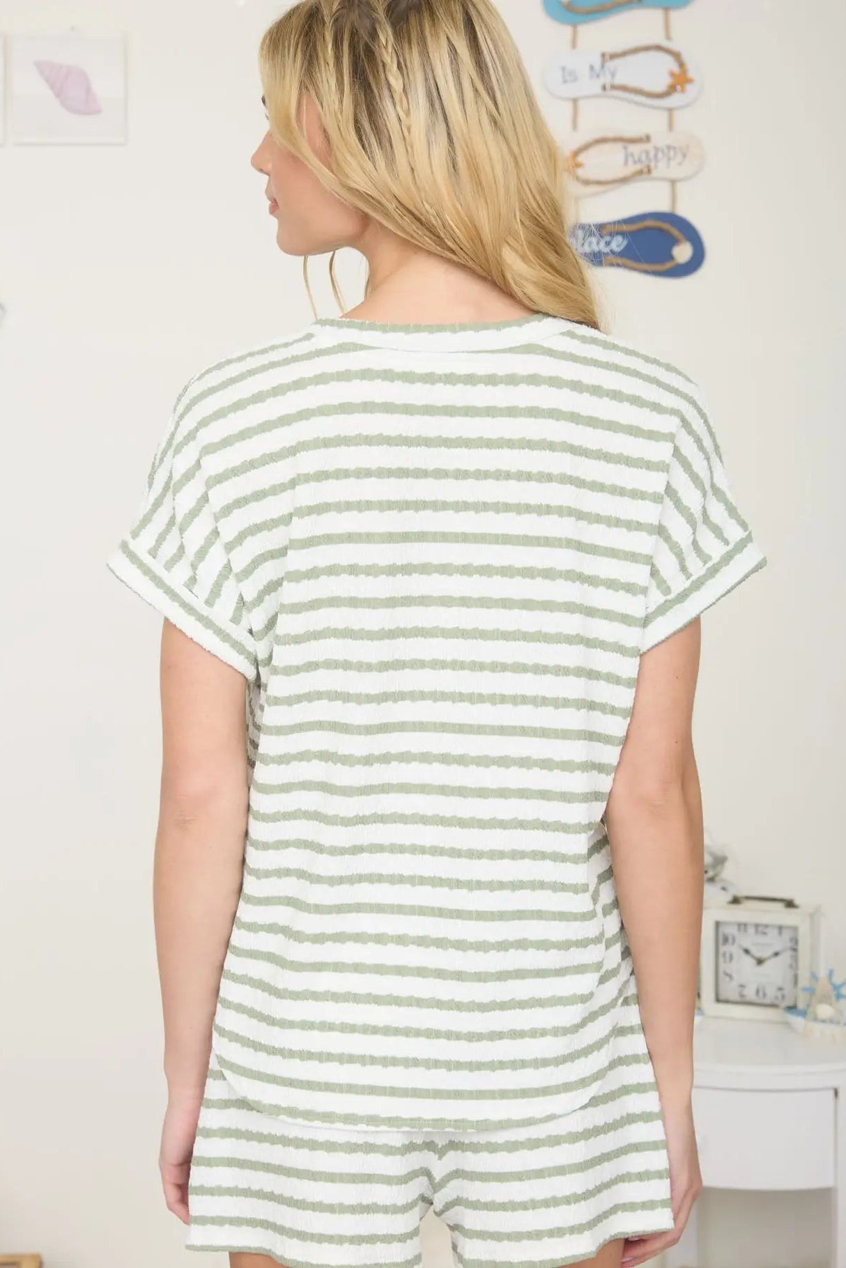 Woman wearing a green and white striped romper in a room with a clock on the wall.
