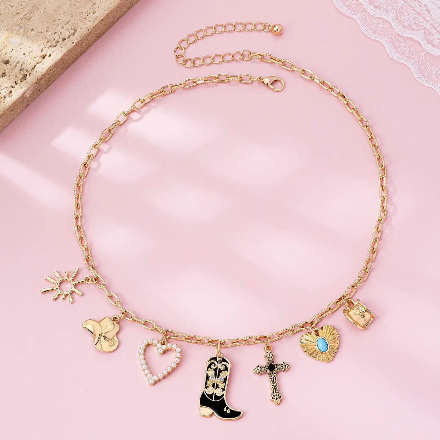 Gold necklace with various charms on a pink surface