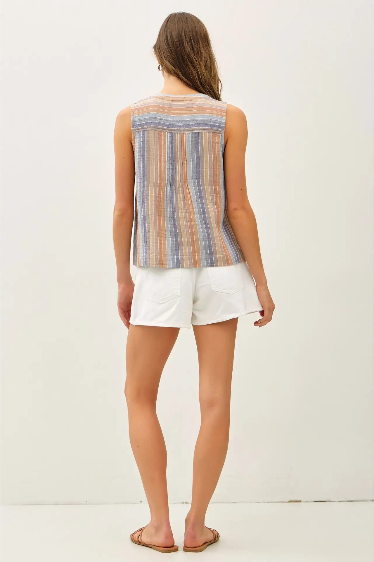 Woman wearing a striped sleeveless top and white shorts on a plain background