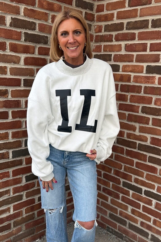 Woman wearing a white sweatshirt with large black letters LL against a brick wall.