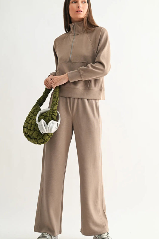 Woman wearing a beige tracksuit holding a green textured handbag on a white background