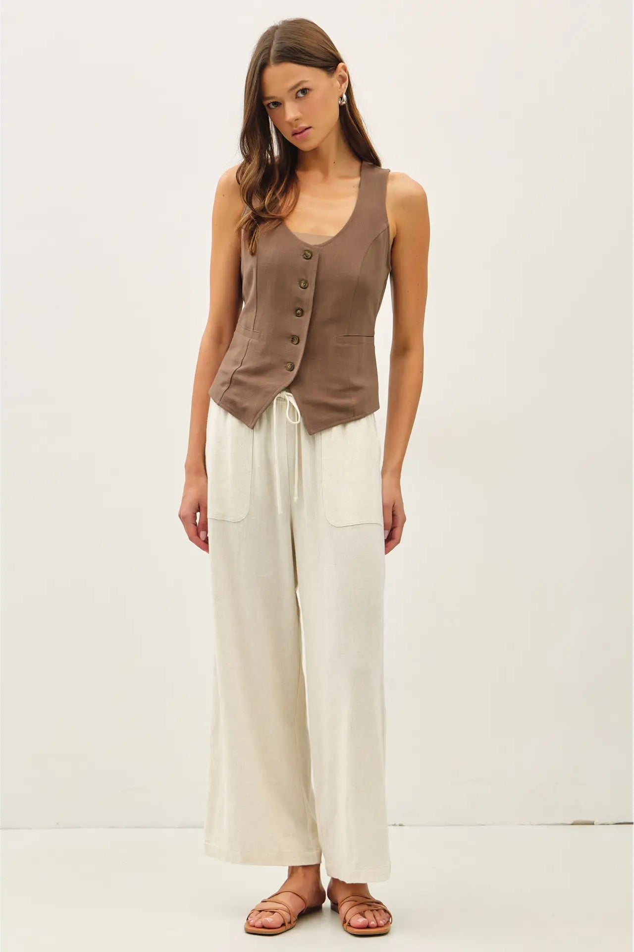 Woman wearing a brown sleeveless top and white pants on a white background