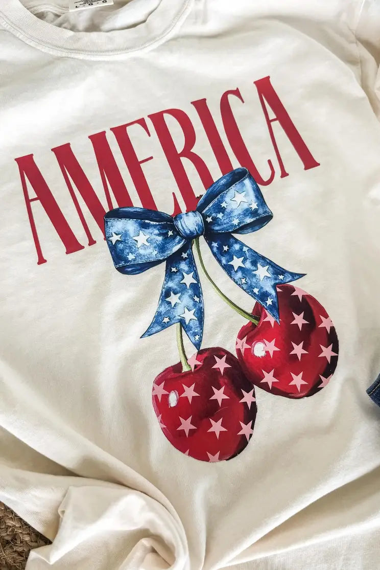White sweatshirt with 'AMERICA' text, blue bow, and red cherries with white stars on a white background.