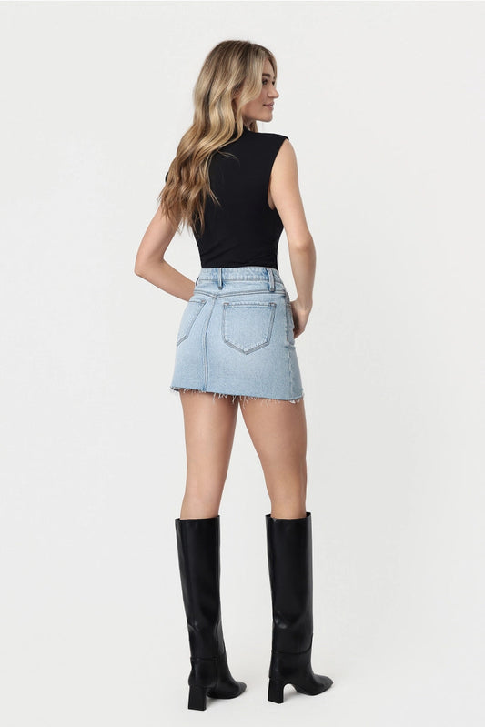 Woman wearing a black sleeveless top, light blue denim skirt, and black knee-high boots on a white background