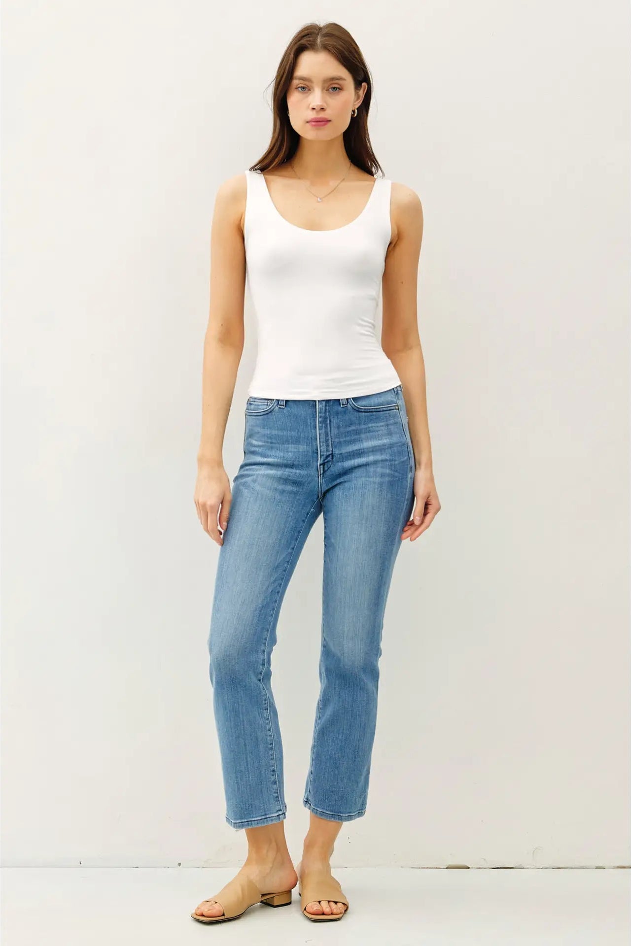 Woman wearing a white tank top and light blue jeans against a plain background