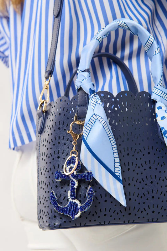 Navy handbag with blue anchor charm and matching scarf, worn by a person in a striped shirt.