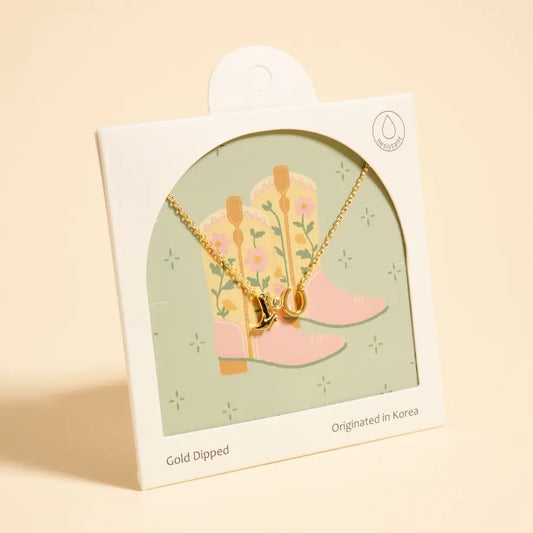 Necklace with pink boot-shaped pendants on a branded card against a beige background