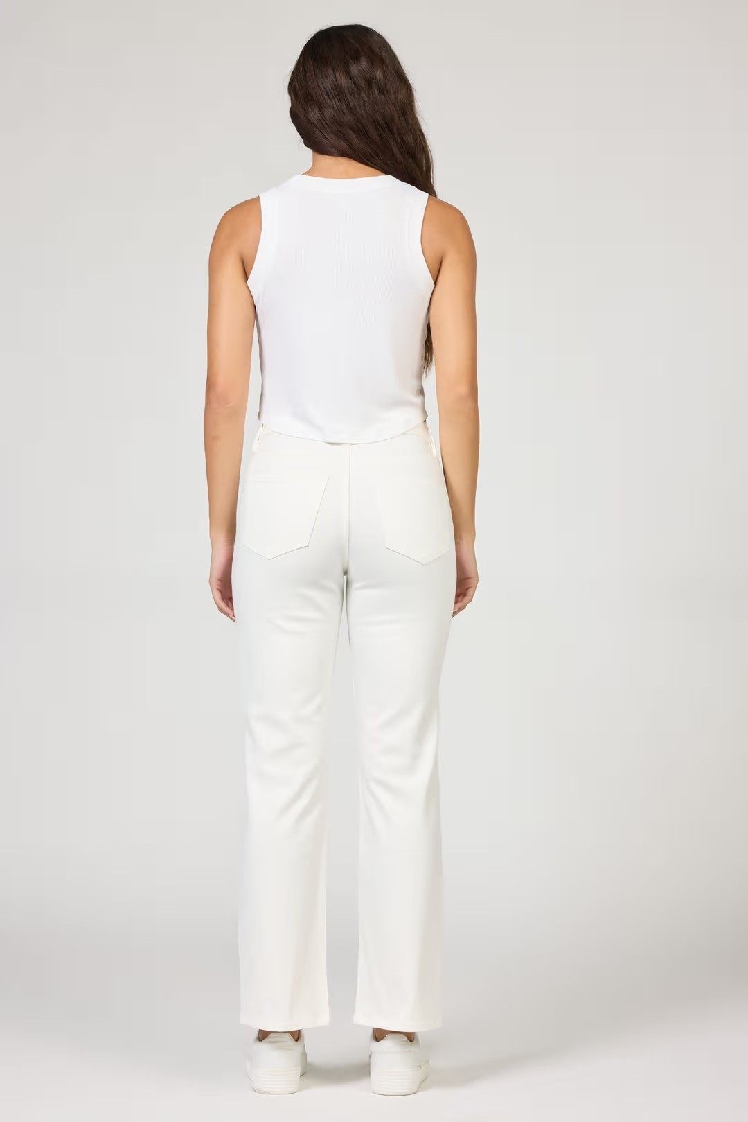 Woman wearing a white sleeveless top and pants on a plain background