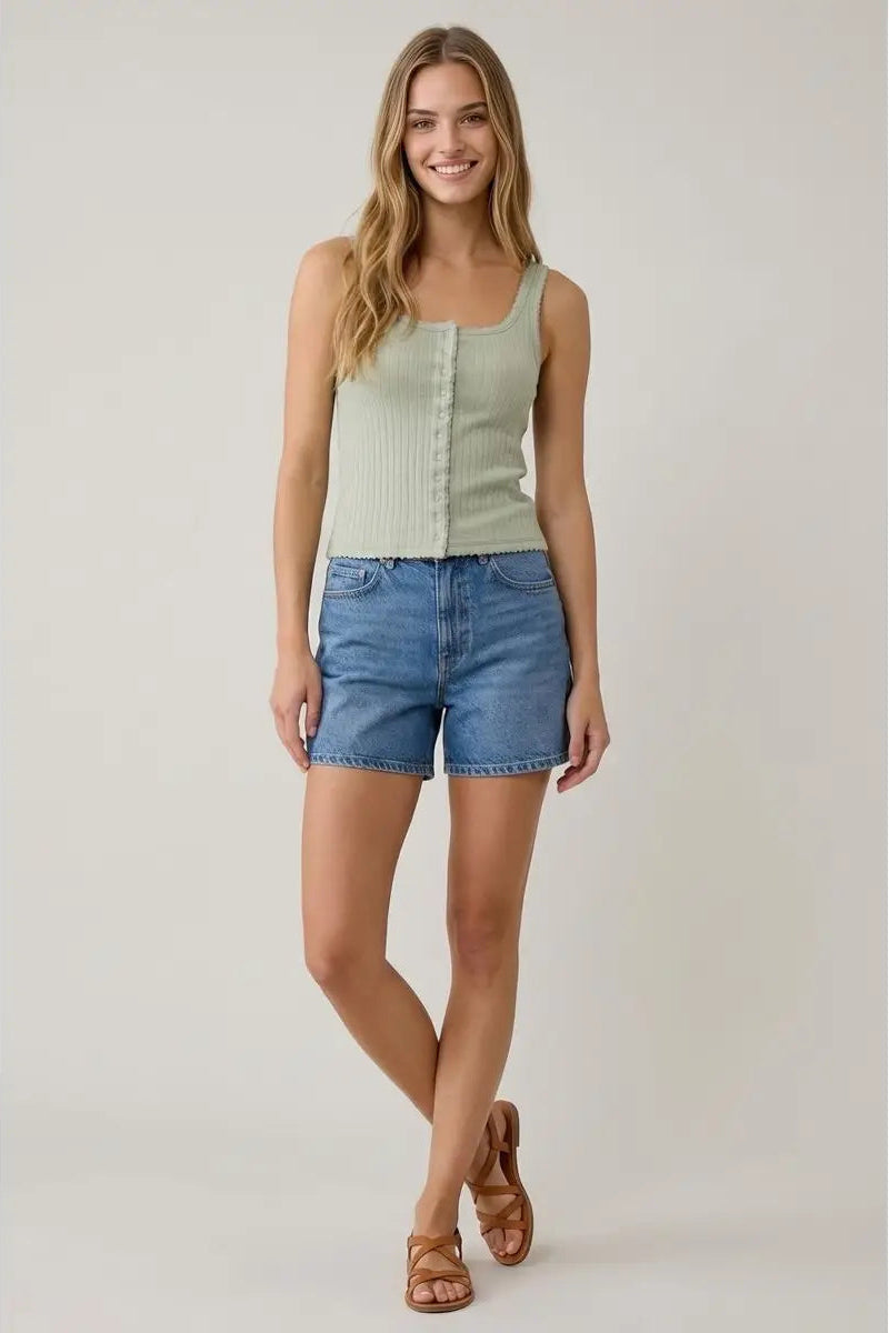 Woman wearing a light green tank top and blue denim shorts on a plain background