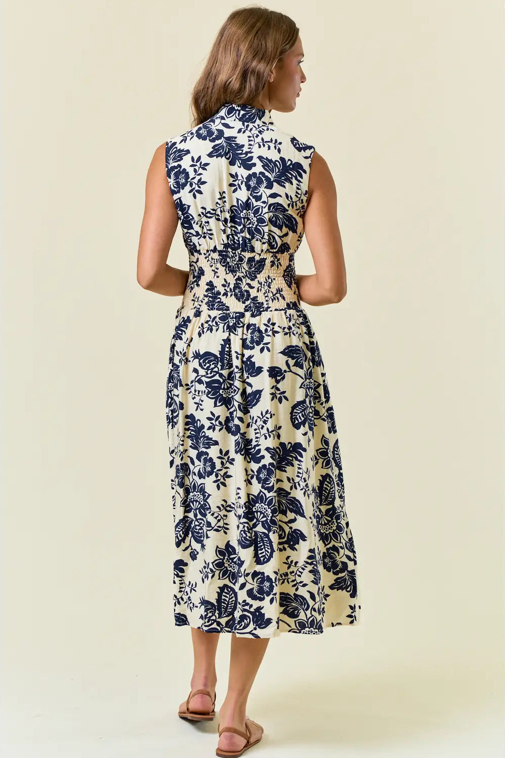 Woman wearing a sleeveless floral dress with blue flowers on a beige background