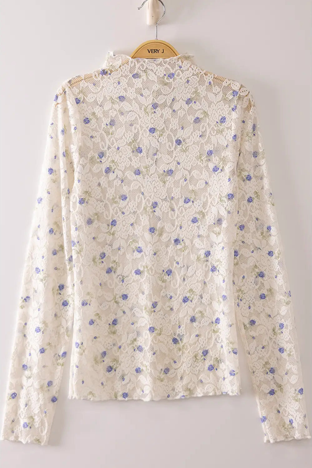 An off-white lace long-sleeve blouse with a blue floral pattern, hanging on a wooden hanger against a light gray background.