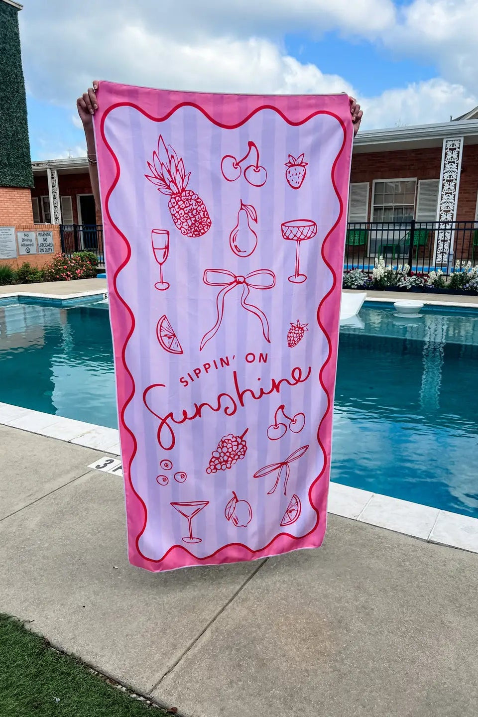 Pink and white beach towel with graphics held by a person by a pool.