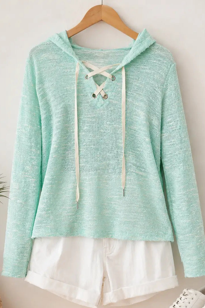 Light blue hoodie with lace-up front on a wooden hanger against a white wall.