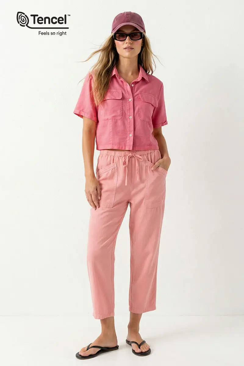 Woman wearing a pink outfit with sunglasses and a cap on a white background, featuring Tencel branding.