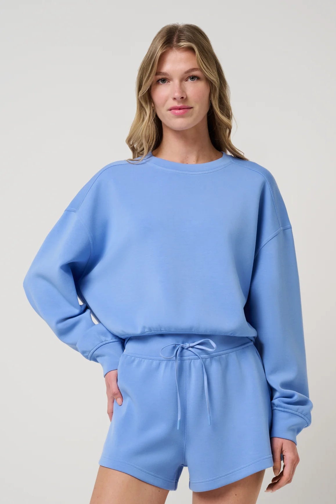 Woman wearing a light blue sweatshirt and shorts set on a plain background