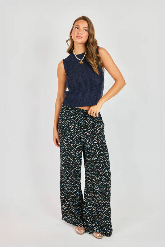 Woman wearing a navy sleeveless top and patterned pants on a white background