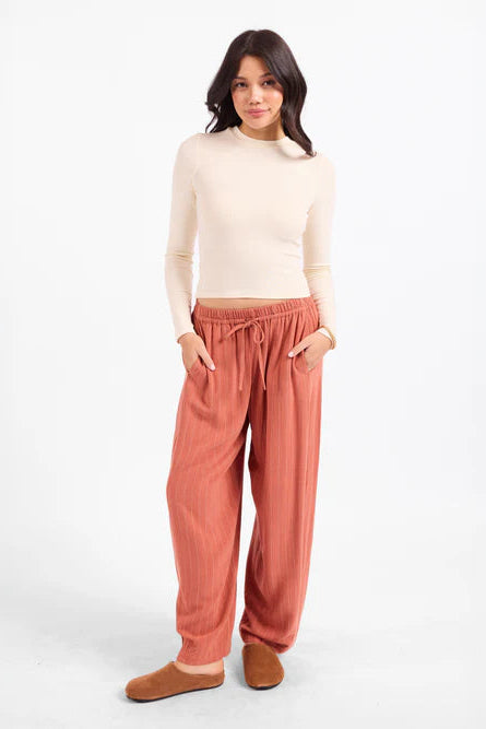 Woman wearing a cream top and rust-colored pants on a white background