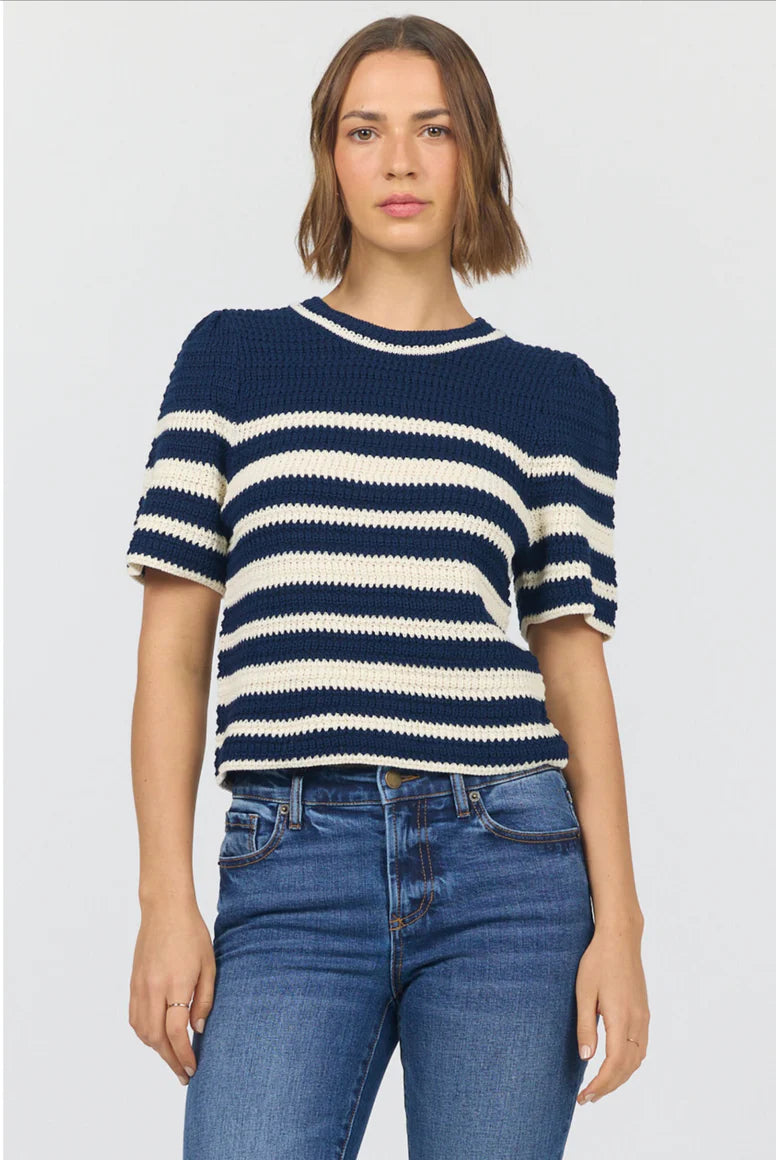 Woman wearing a navy and white striped sweater with blue jeans on a light gray background