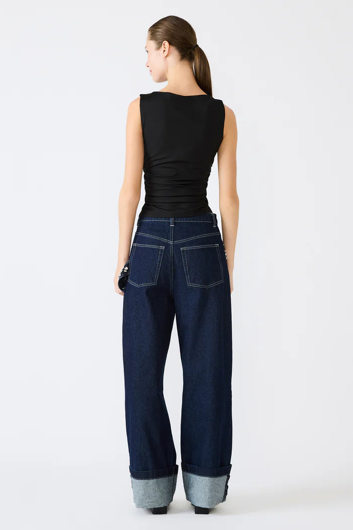 Woman wearing dark blue wide-leg jeans and a black sleeveless top on a white background