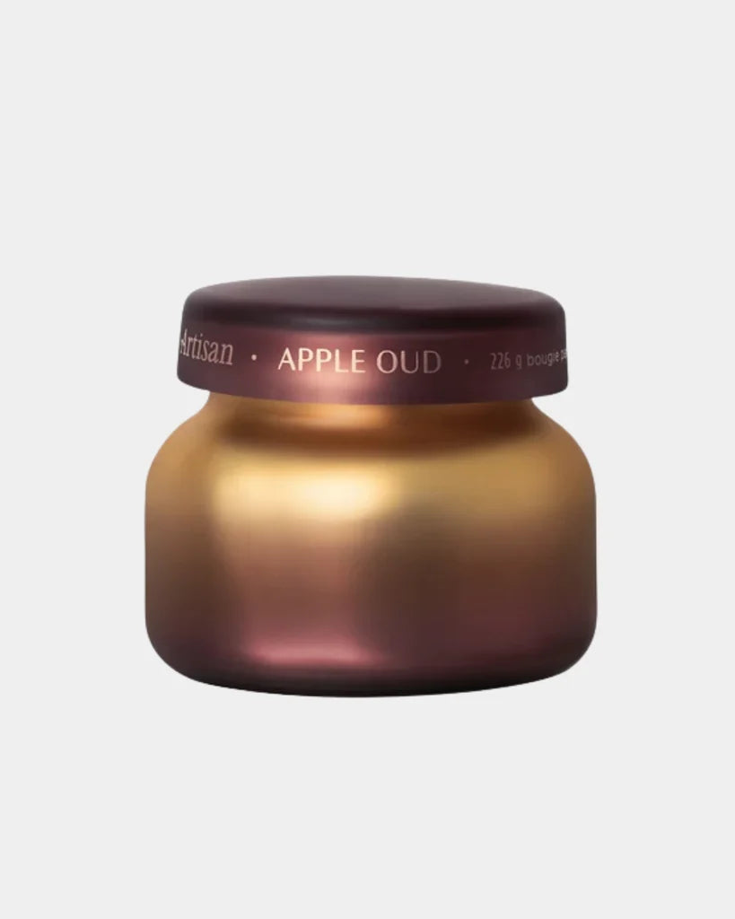 A frosted glass cosmetic jar with a metallic gradient transitioning from deep burgundy to warm gold, featuring a matching dark burgundy lid with white text that reads 'Artisan • APPLE OUD'.