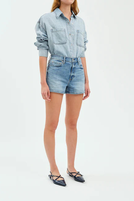 Person wearing a light blue denim shirt and shorts on a white background