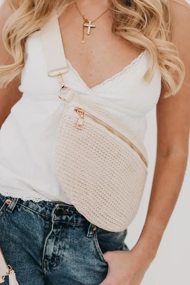 Woman wearing a white sleeveless top and blue jeans, holding a beige woven bag.
