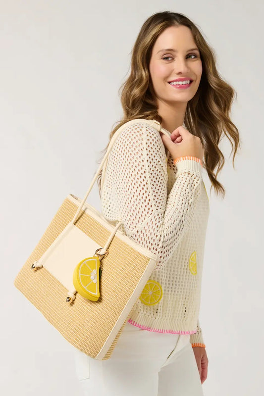 Woman holding a straw bag with lemon decorations against a plain background