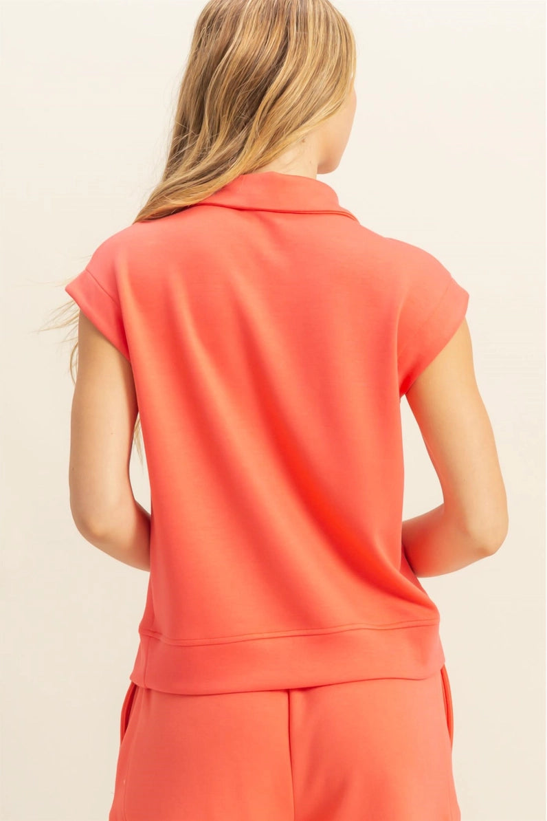 Person wearing a coral sleeveless top and pants on a beige background