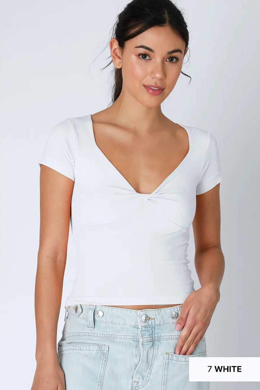 Woman wearing a white crop top and light blue jeans on a plain background