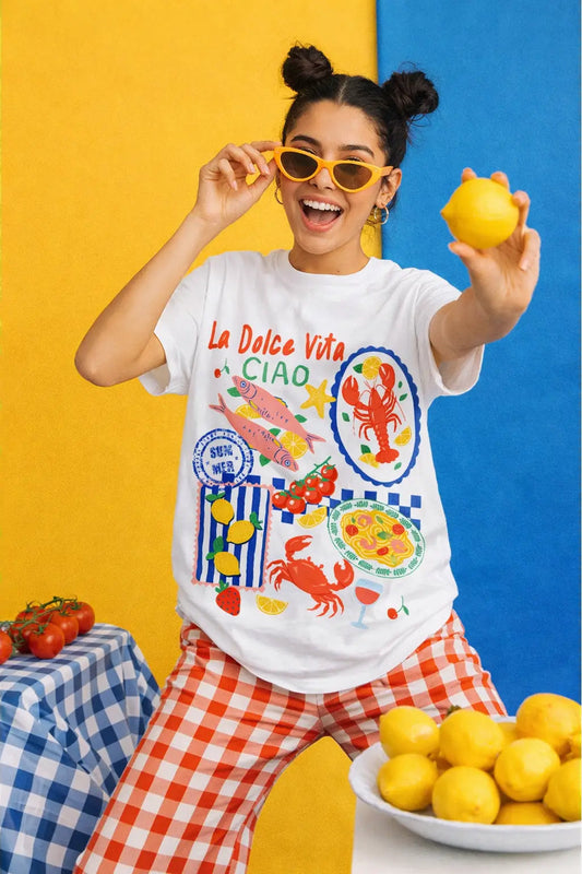 Woman wearing a colorful graphic t-shirt with a lemon-themed design, standing against a yellow and blue background.