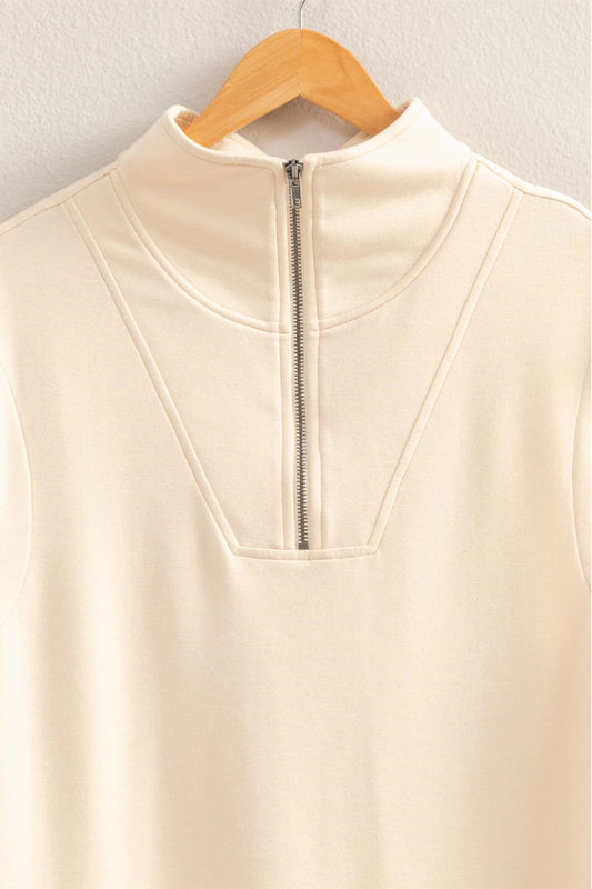 Beige sleeveless top with a zipper on a wooden hanger against a light gray background